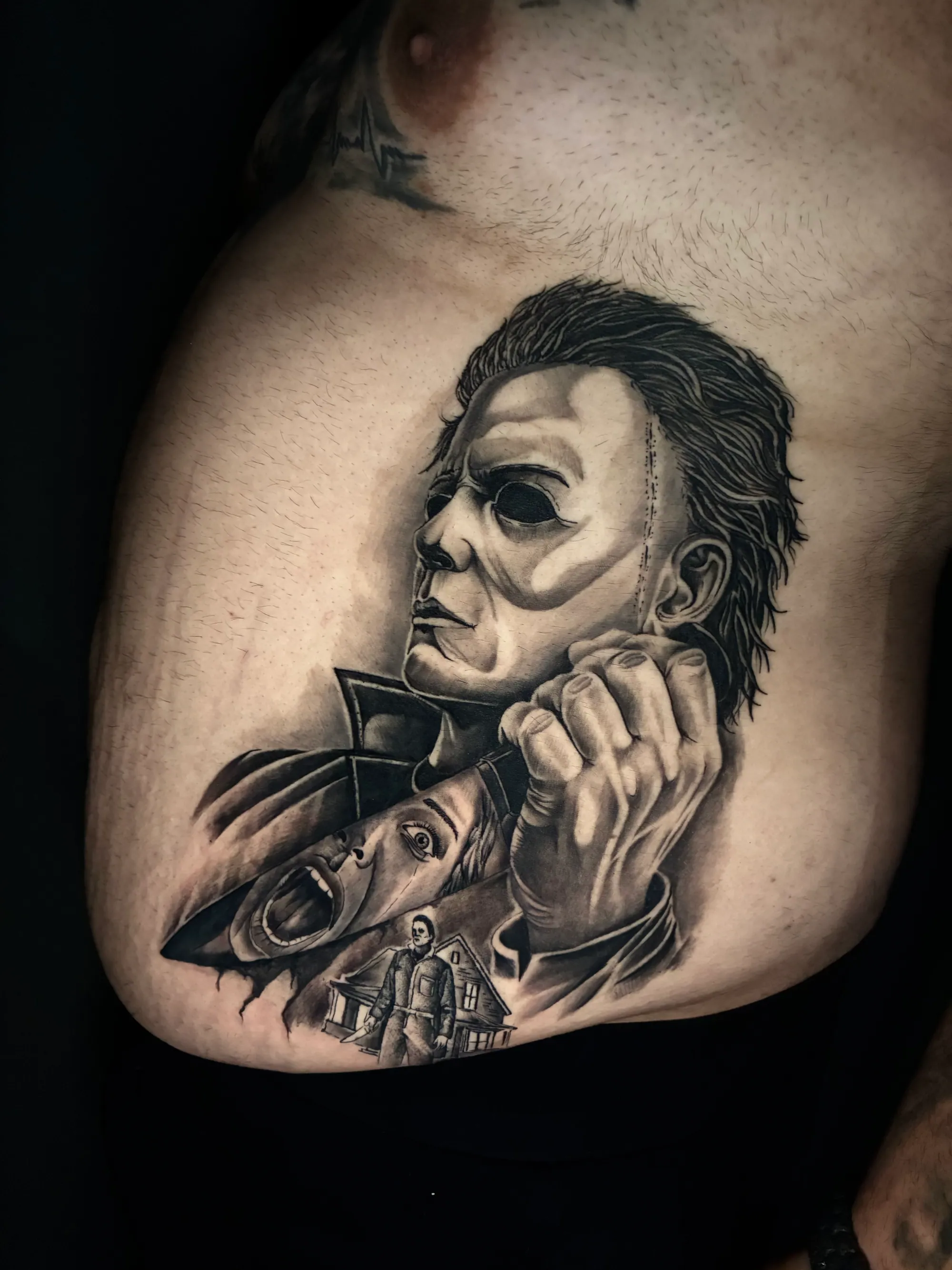 Realistična crno-bela tetovaža horor scene sa maskiranim likom i  kućom u pozadini na ramenu, Dropz Tattoo Studio Niš