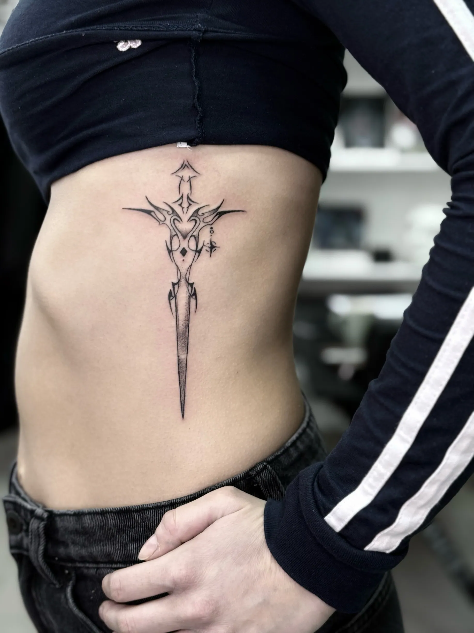 Fine line tetovaža ornamentalnog bodeža sa tribal elementima na  rebrima, Dropz Tattoo Studio Niš