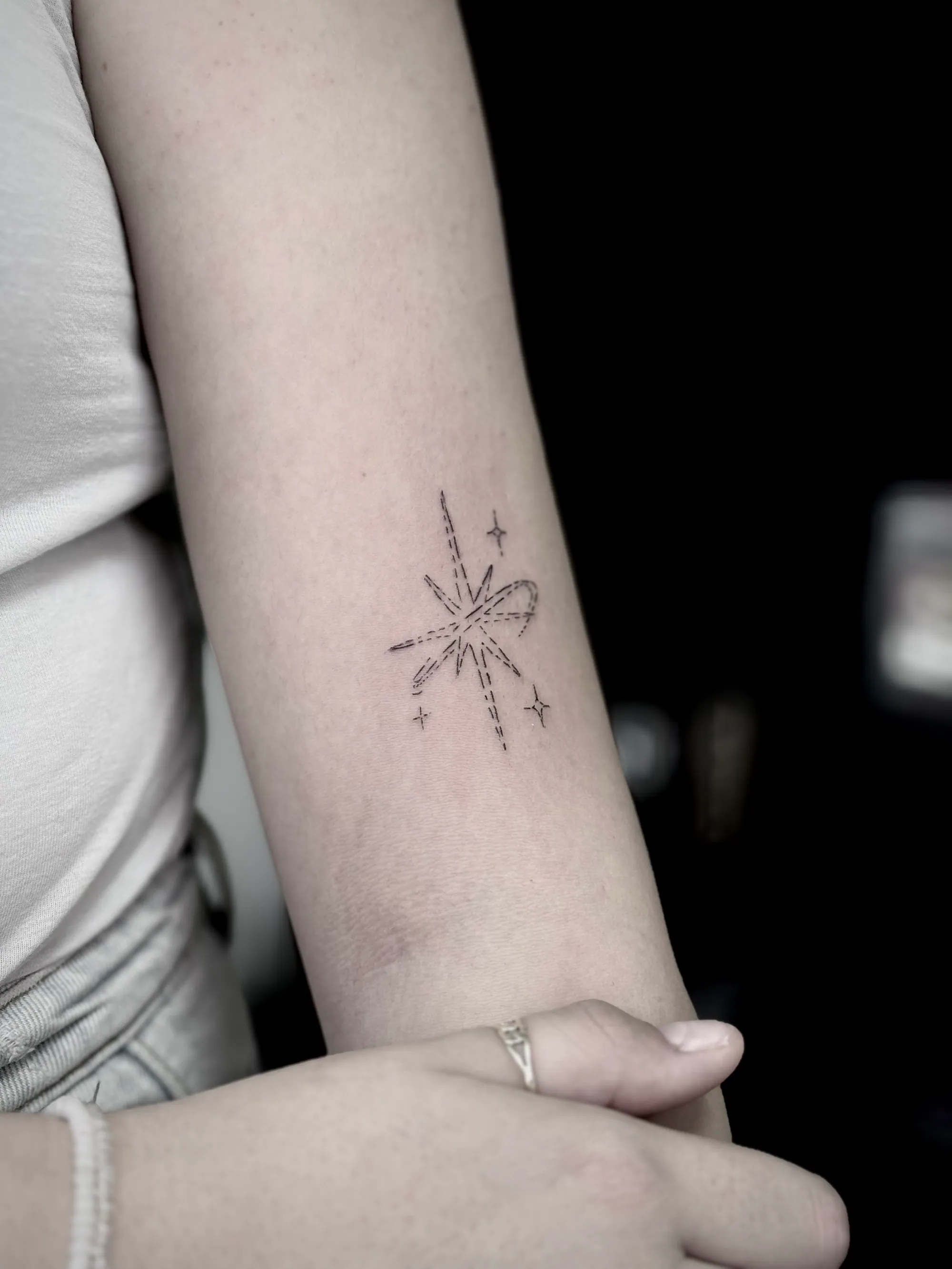Fine line minimalistička tetovaža zvezde eksplozije sa mašnicom  na podlaktici, Dropz Tattoo Studio Niš
